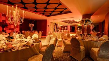 A banquet hall with round tables, white tablecloths, and chairs with white covers.