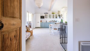 Una cocina moderna con armarios blancos, un comedor con sillas blancas y una puerta de madera.