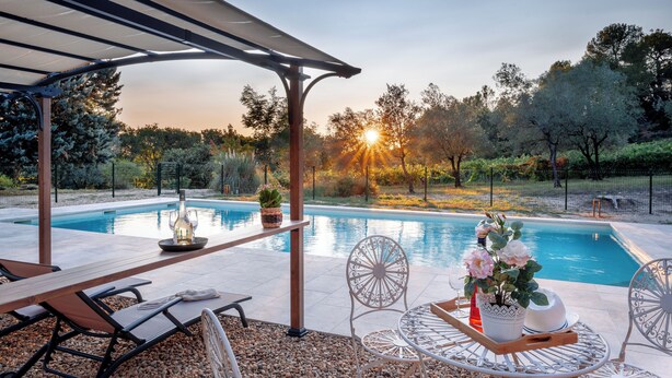 Zona junto a la piscina con una pérgola, asientos y una mesa con una planta en maceta.