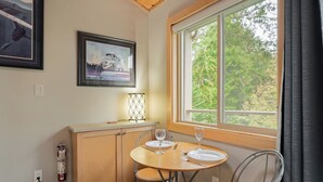 Un comedor con mesa de madera, sillas de metal y ventana con vista a árboles.