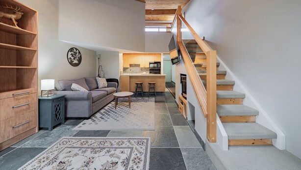 Un interior moderno con una escalera de madera, una cocina y una sala de estar con sofá y alfombra.