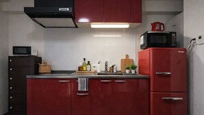 A compact kitchen with red cabinetry, a microwave, a Gengle refrigerator, and a small sink area. - DOUTONBORI Sleeps up to 5 w 2 beds 1 sofa bed Convenient land (大阪市)