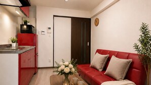 A compact living space with a kitchenette, a red sofa, a coffee table with decorative items, and a potted plant. - DOUTONBORI Sleeps up to 5 w 2 beds 1 sofa bed Convenient land (大阪市)