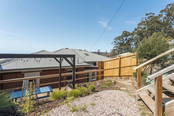 A two-story building with a metal roof, a wooden fence, and a gravel driveway. - Modern 3-Bed Coastal Escape (Burnie)