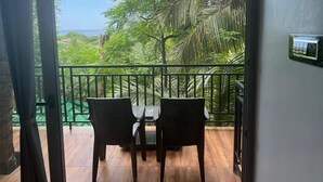 Un balcone con due sedie e un tavolo, vista su un rigoglioso giardino e l'oceano.