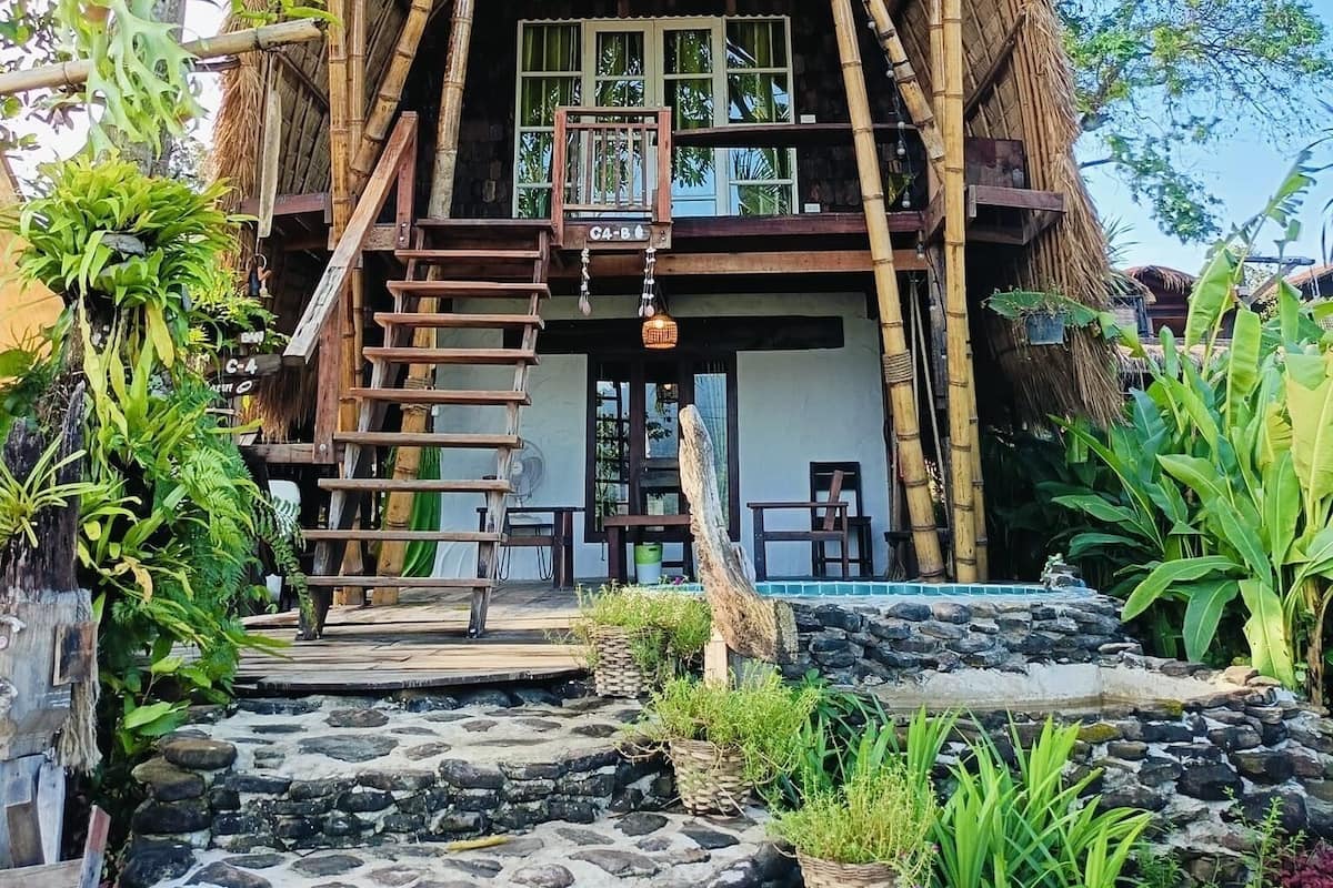A traditional thatched-roof house with a wooden staircase leading to a balcony.