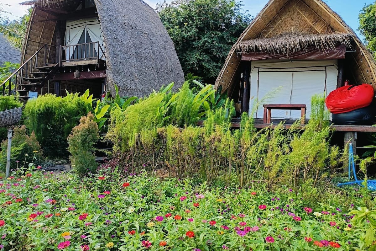 A traditional thatched-roof house with a balcony and a garden with colorful flowers.