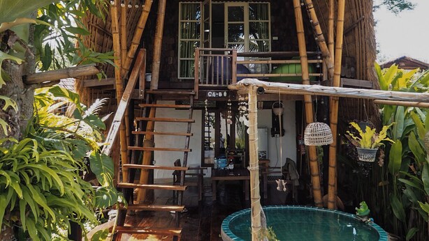 Una casa di bambù con tetto di paglia, una scala in legno e una piccola piscina.