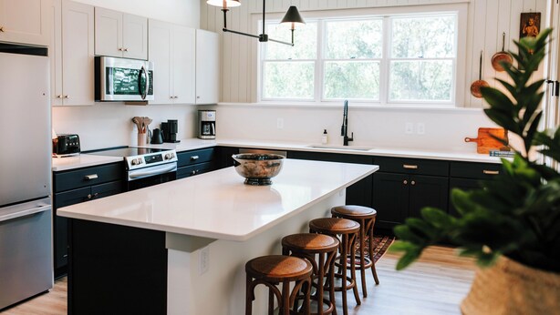 A modern kitchen with white cabinets, a central island with stools, a microwave, stove, and a large window. - Upscale 2BR Apartment by MHM Luxury Properties (Athens)