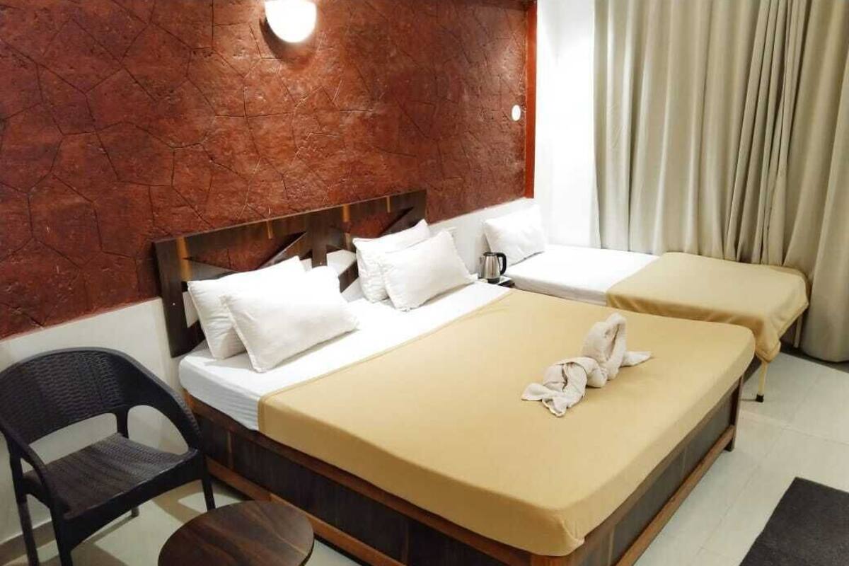 A hotel room with a large bed, a smaller bed, a chair, a table, and a wall-mounted light fixture.