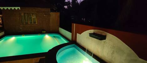 Dos piscinas con fuentes, rodeadas por un edificio de ladrillo y palmeras.