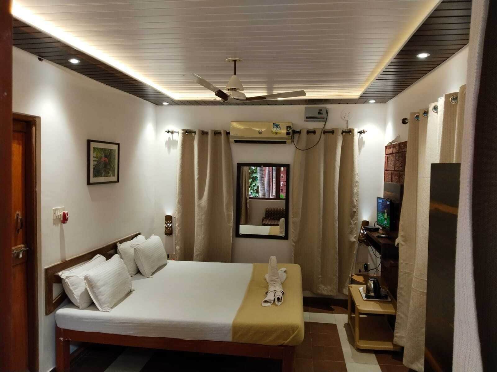 Une chambre d’hôtel équipée d’un lit, d’un bureau avec un ordinateur, d’une télévision et d’un ventilateur de plafond.