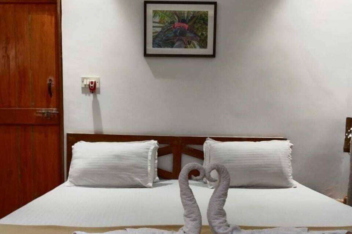 A hotel room with a bed, two pillows, a framed picture on the wall, and a towel arranged in a swan shape on the bed.