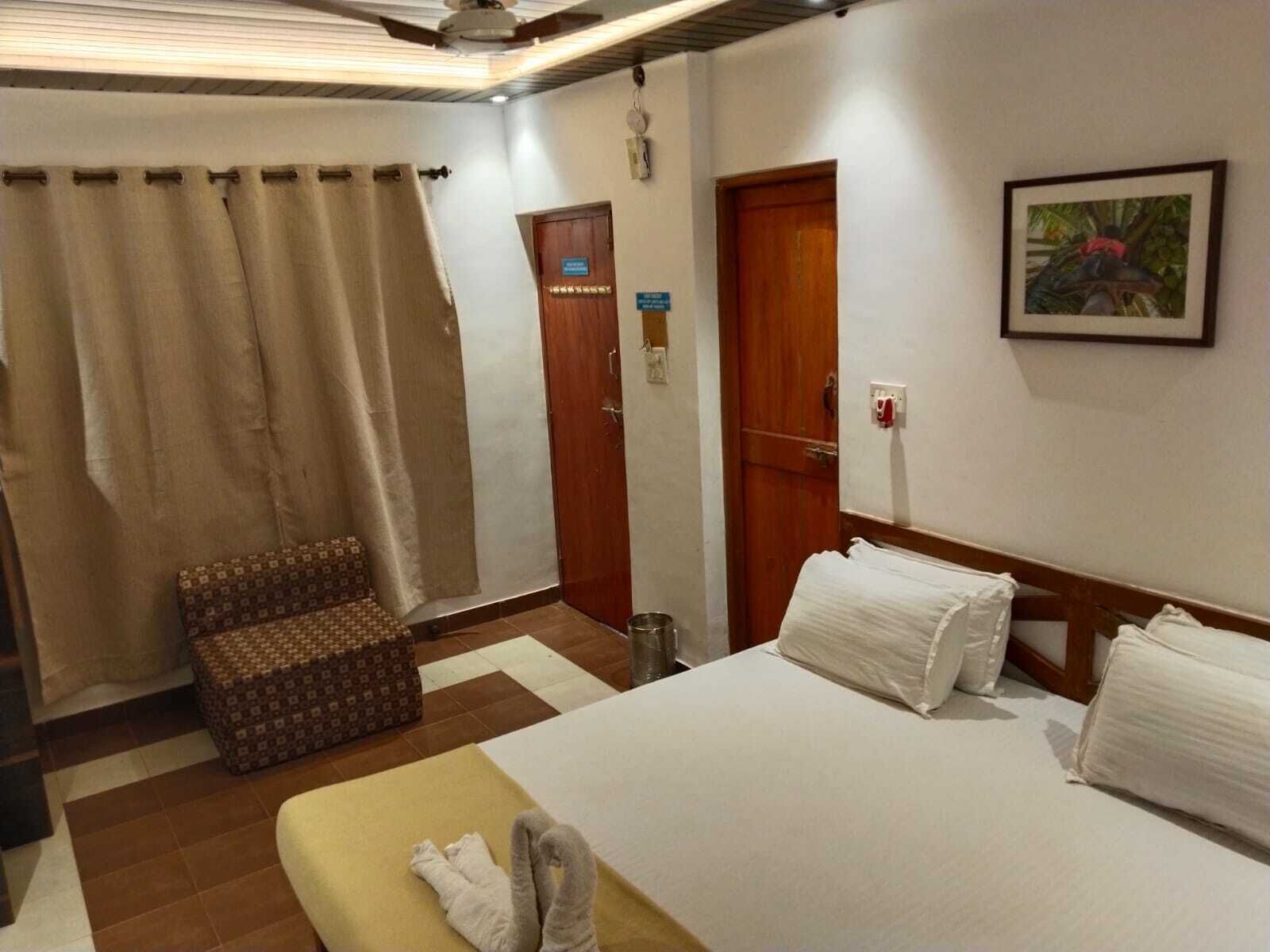 A hotel room with a bed, a small sofa, a wooden door, and a framed picture on the wall.