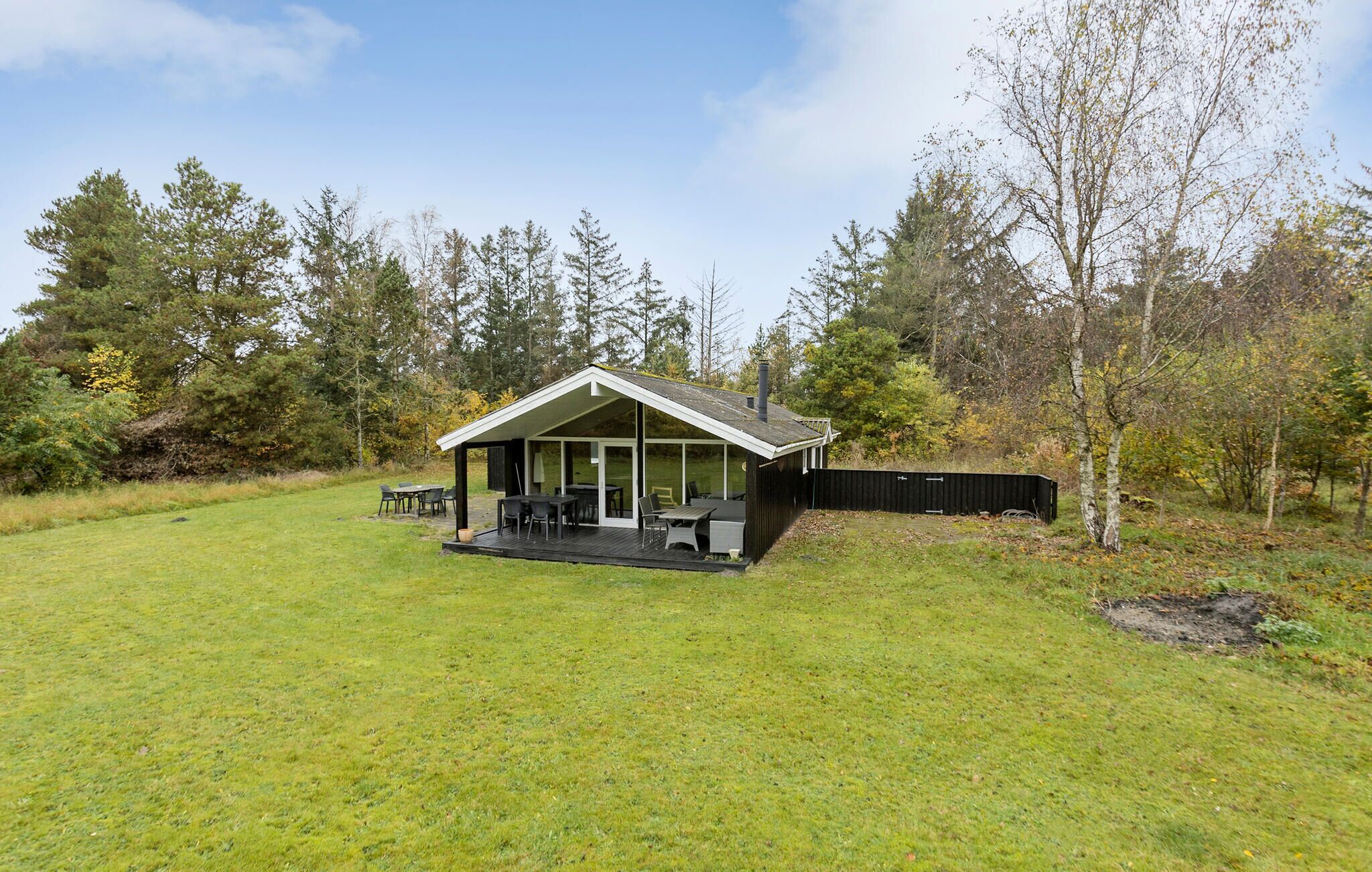 A small cabin with a covered patio and a deck, surrounded by a grassy yard and trees.