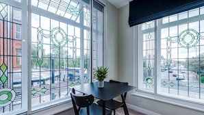 A room with two large windows featuring intricate stained glass designs, a black table with a potted plant, and black chairs. - Contemporary 1BR Gem | Elysée Suites, Southport (Southport)