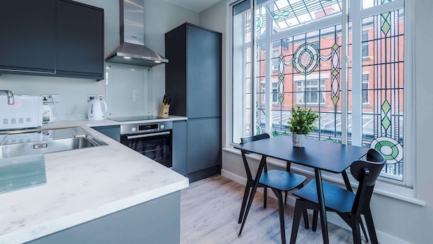 A modern kitchen with grey cabinets, a stainless steel range hood, and a large window with stained glass. - Contemporary 1BR Gem | Elysée Suites, Southport (Southport)