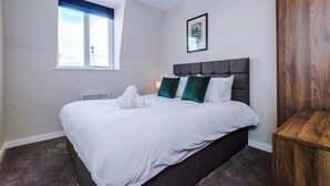 A hotel room with a large bed, a window with a view, a framed picture on the wall, and a wooden nightstand.