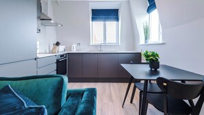 A modern kitchen with a dining area, featuring a black dining table, a green sofa, and a potted plant.