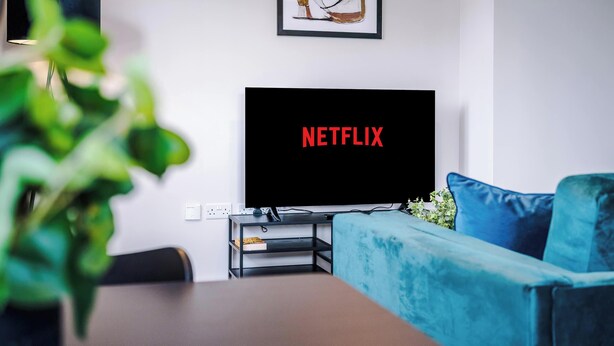 A modern living room with a flat-screen TV displaying "NETFLIX," a blue sofa, a small side table, and a framed abstract painting on the wall.