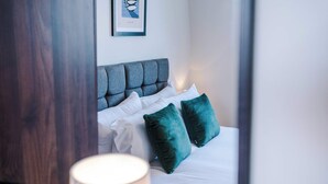 A neatly made bed with white linens and two teal pillows, a grey upholstered headboard, and a framed picture on the wall. - Elysée Suites - Chic 1 Bed Flat in Southport (Southport)