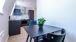A modern kitchen with dark cabinetry, a microwave, and a stove. There is a dining table with chairs and a potted plant. - Elysée Suites - Chic 1 Bed Flat in Southport (Southport)