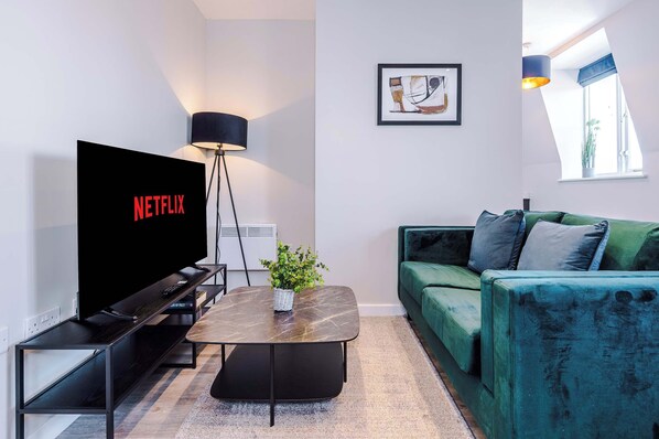 A modern living room with a flat-screen TV, a floor lamp, a green sofa, and a framed abstract painting on the wall.