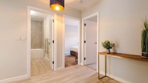 A hallway with wooden flooring, white walls, and a gold-framed console table with a potted plant.