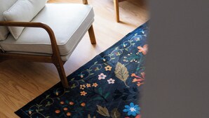 A room with a wooden floor, a white chair with a cushion, and a floral-patterned rug.