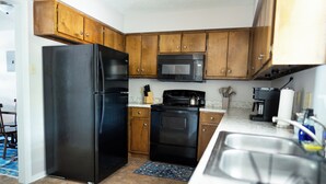 A kitchen with wooden cabinets, a black refrigerator, a microwave, an oven, and a sink.