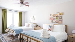 A hotel room with two beds, a ceiling fan, a nightstand, and a wall with framed pictures.
