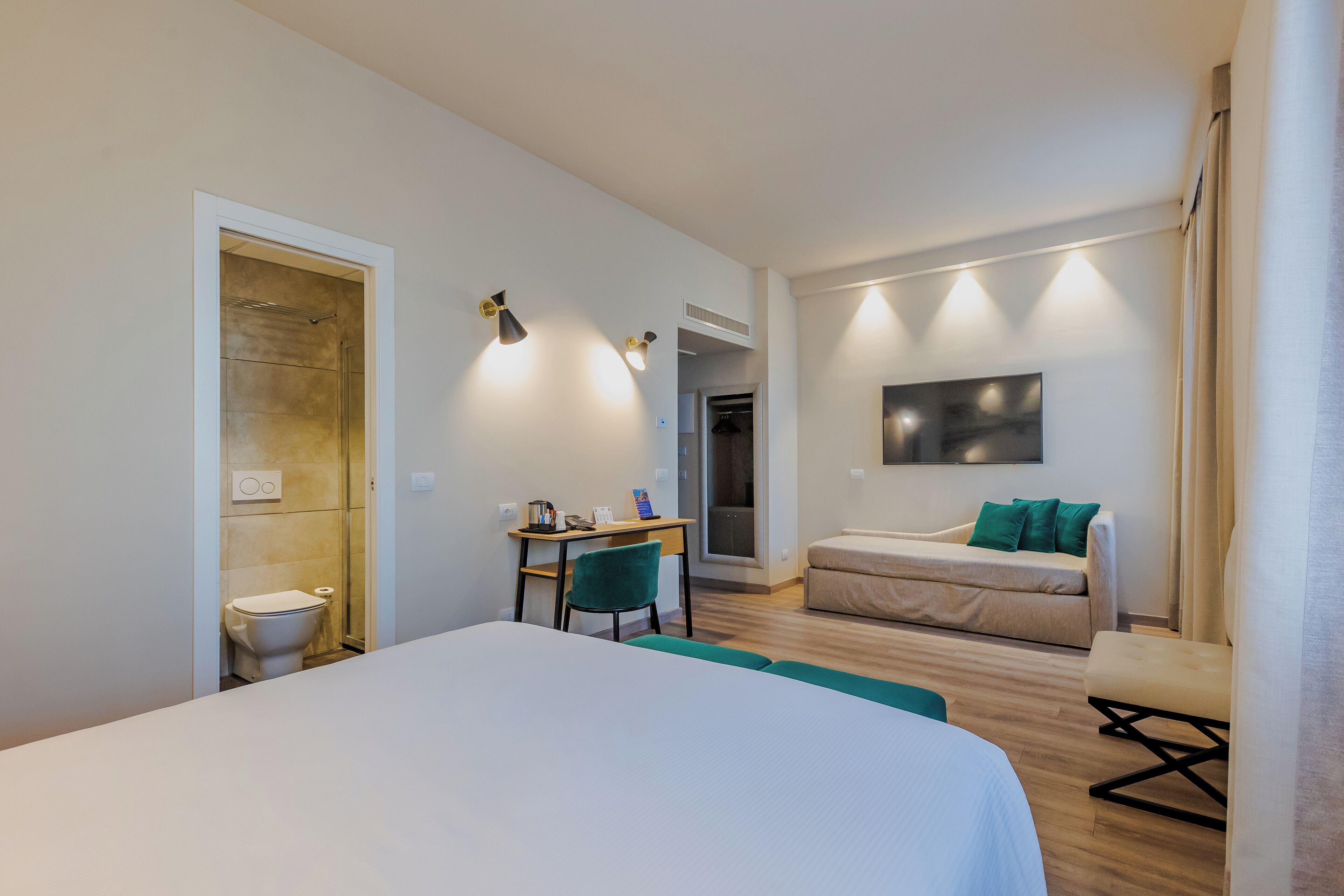 A hotel room with a bed, a desk, a chair, a sofa, and a TV.