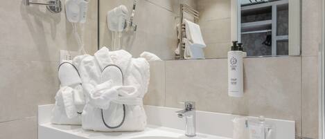 A modern bathroom with a white sink, a round mirror, a hairdryer, and a towel rack.