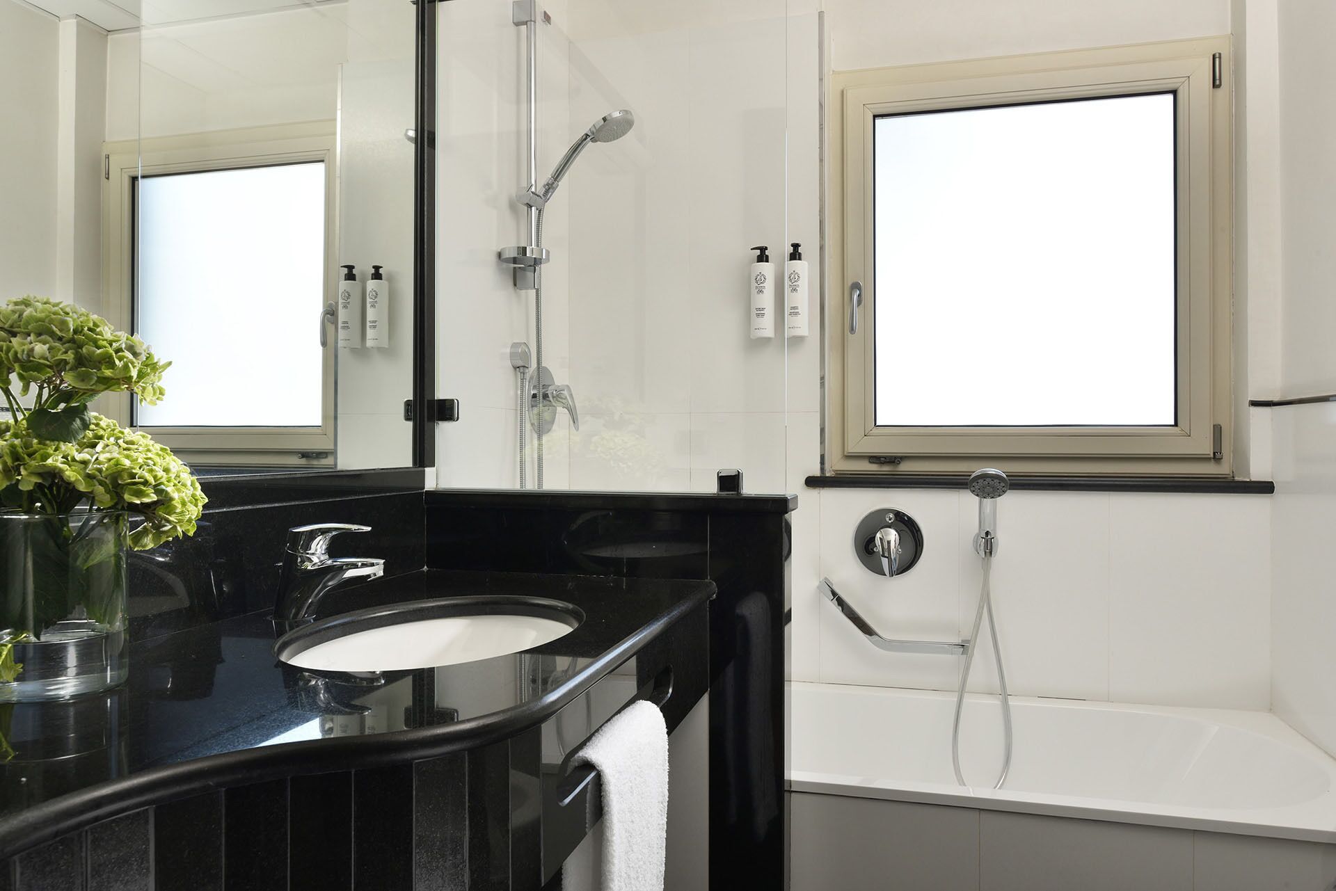 Un baño moderno con tocador negro, cabina de ducha de vidrio y bañera blanca.