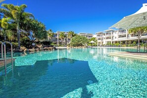 En klarblå pool omgiven av palmer och en hotellbyggnad med flera balkonger.