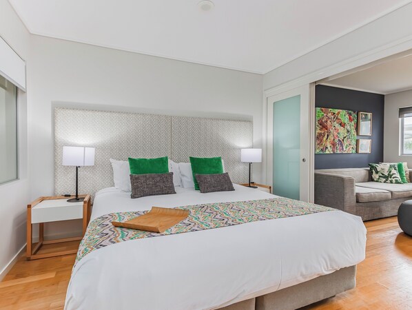 Ett modernt hotellrum med en stor säng, två sängbord, ett litet bord, en soffa och en färgstark, abstrakt tavla på väggen.
