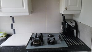 A kitchen with white cabinets, a gas stove, and a coffee maker. - Kosy Roomz  - Rooms Only (Welling)