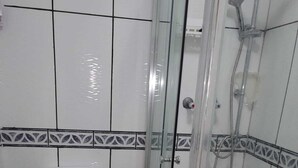 A bathroom with a toilet, a shower with a glass door, and patterned tiles. - Kosy Roomz  - Rooms Only (Welling)