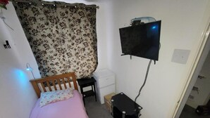 A small bedroom with a single bed, a desk, a chair, a television mounted on the wall, and a small cabinet. - Kosy Roomz  - Rooms Only (Welling)