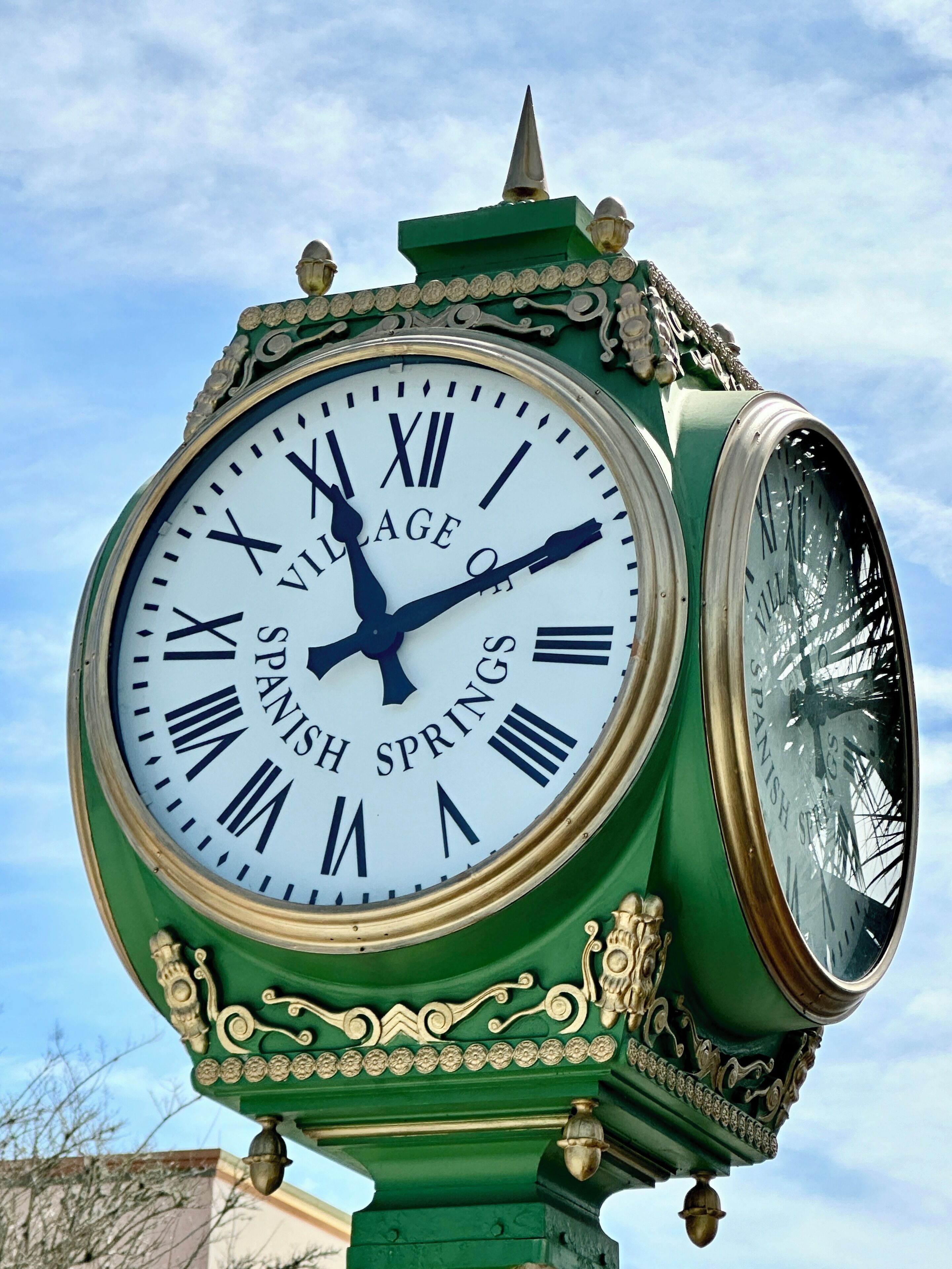 Une grande horloge décorative, ornée de chiffres romains et portant l’inscription « VILLAGE DE SPANISH SPRINGS ».