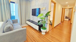 Een moderne woonkamer met een grijze bank, een flatscreen televisie aan de muur, een potplant en houten vloeren.