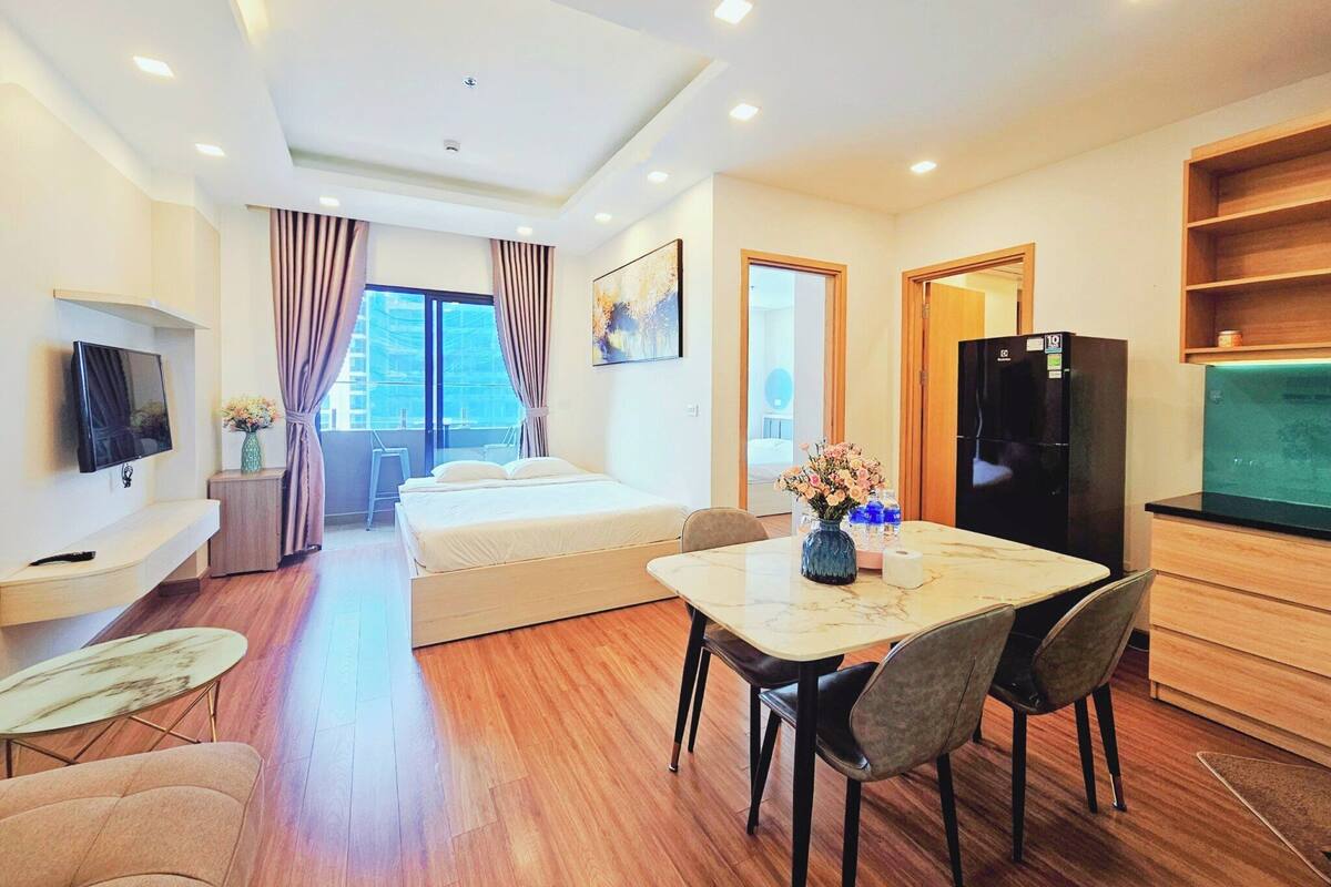 Una habitación de hotel moderna con una cama, un comedor con mesa y sillas, un televisor montado en la pared y un refrigerador.