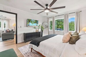 A bedroom with a bed, ceiling fan, large windows, and a view of the outdoors.