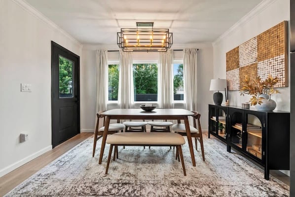 A dining area with a table, chairs, a bench, a chandelier, a black console, and a decorative wall piece.