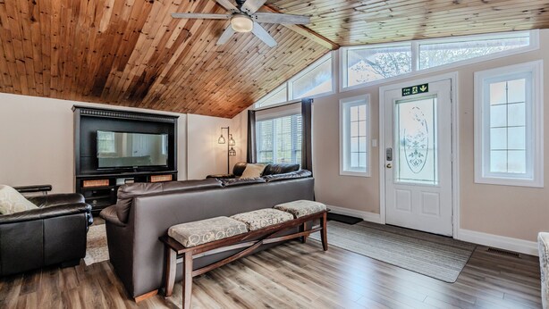 Un salon spacieux avec un grand canapé d’angle, un téléviseur à écran plat, un plancher en bois et un ventilateur de plafond.