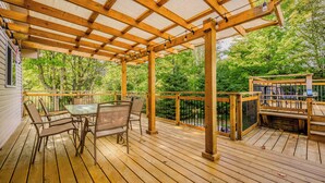 Une terrasse en bois agrémentée d’une pergola, d’un espace salon extérieur et offrant une vue sur une zone boisée.