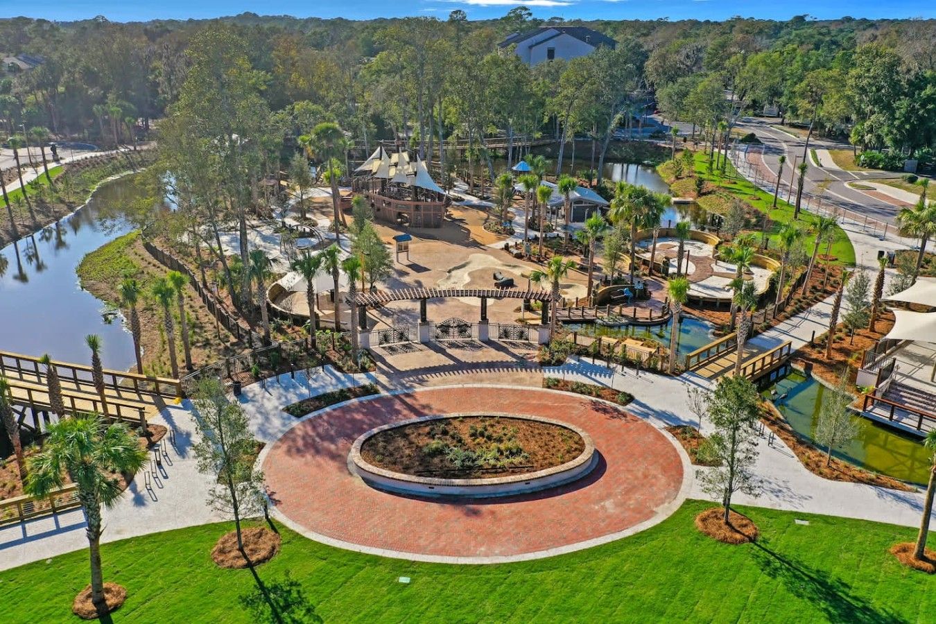 A resort with a central circular water feature, surrounded by pathways, palm trees, and a lake.