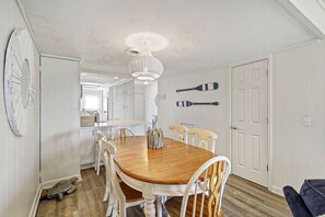 Un comedor con una mesa y sillas de madera, una araña y vista a la cocina.