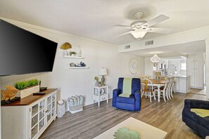 A spacious living room with a flat-screen TV, a ceiling fan, and a dining area with a wooden table and chairs.