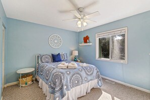 A bedroom with a bed, a ceiling fan, a window, and a decorative wall piece.